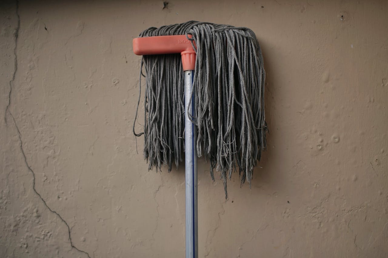 Gray mop leaning against a textured wall, conveying simplicity in a domestic setting.